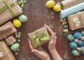 A young woman holds a gift in her hands. Colored eggs and holiday symbols on a dark wooden table. Zero waste concept.
