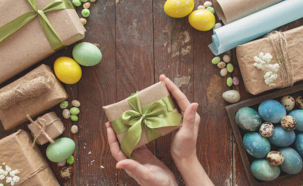 A young woman holds a gift in her hands. Colored eggs and holiday symbols on a dark wooden table. Zero waste concept.